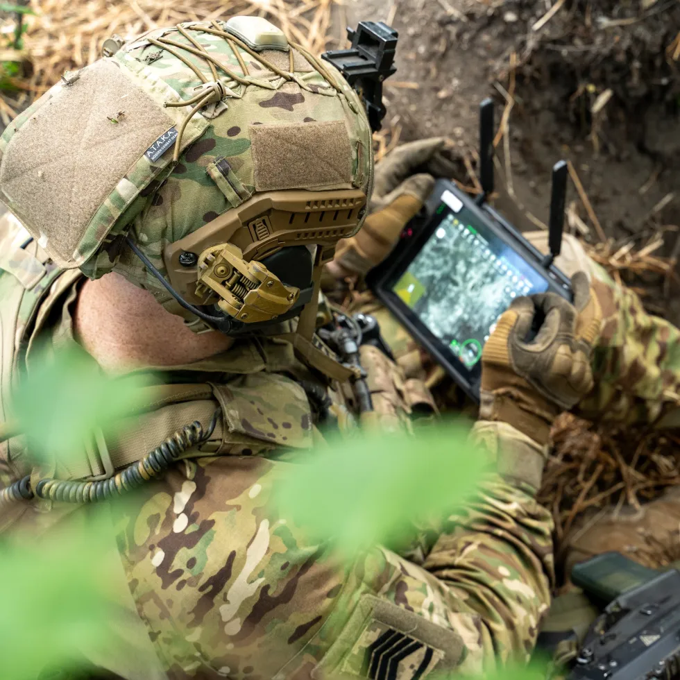 A picture of a soldier looking at a screen in a field