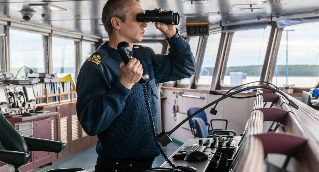 Deck officer with binoculars on navigational bridge. Seaman on board of vessel. Commercial shipping. Cargo ship.