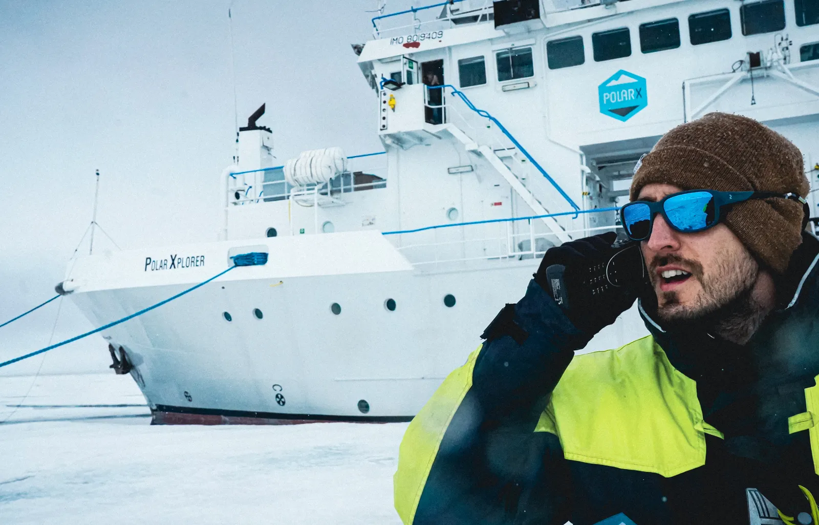 Person in winter clothing holding a device and standing next to a large vessel.