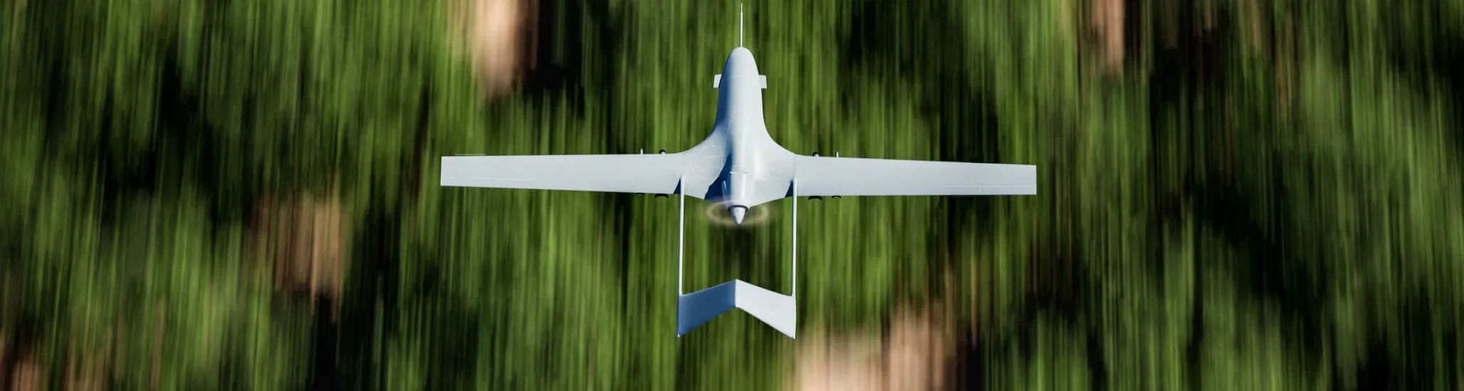 Top shot of a military UAV or drone (Bayraktar TB2) armed with missiles and flying over forest area with the ground blurred