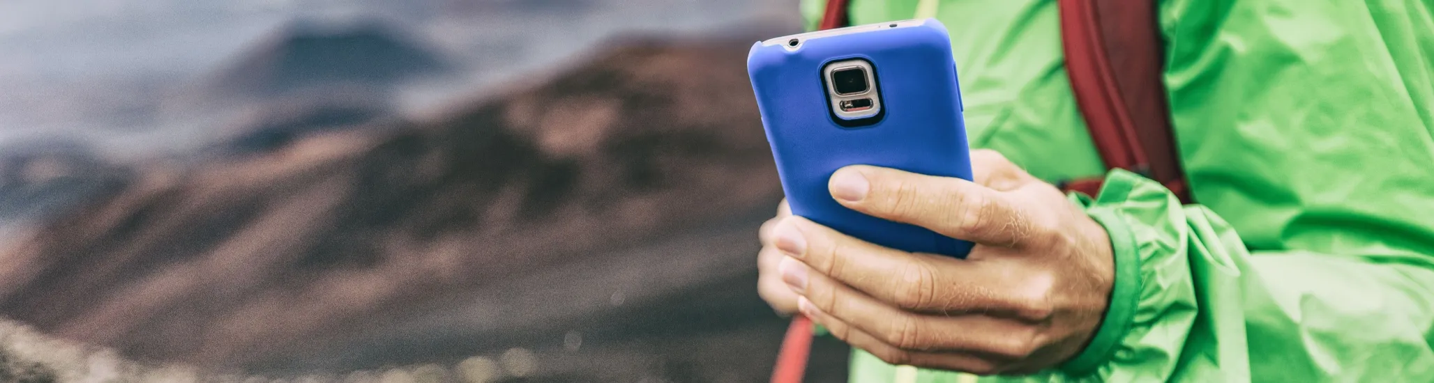 Phone man texting during trek hike in volcano mountain. Young person on travel lifestyle using his smartphone online.