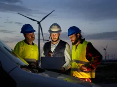 Group of engineers in discussed the plan for the maintenance of wind turbines working with a laptop in a field wind turbines power station. Renewable and clean energy concept, sustainable future