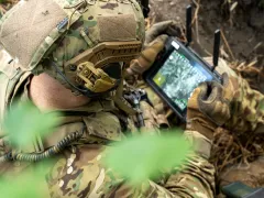 A picture of a soldier looking at a screen in a field