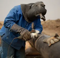 Persone with helmet and gloves, welding a pipe