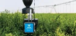 A close-up of a Valley Aqua Trac Lite agricultural sensor mounted above a field of green crops, with an irrigation pivot structure visible in the blurred background.