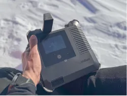 Hand holding an Iridium GO! exec satellite communication device against a snowy Antarctic backdrop.