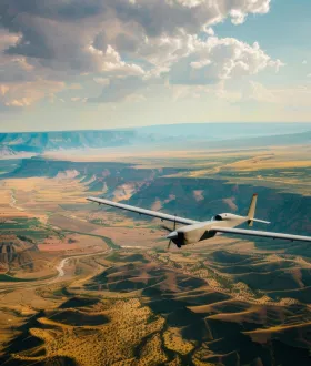 Top shot of a military UAV or drone (Bayraktar TB2) armed with missiles and flying over forest area with the ground blurred