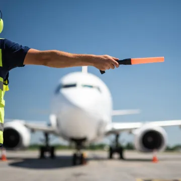 Important signal. Back view of airport worker meeting aircraft and showing right position for landing