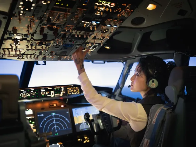 Rear view of a female pilot adjusting switches on the control panel while sitting inside cockpit. Woman operating the switches while flying an airplane.