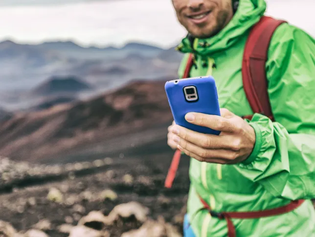 Phone man texting during trek hike in volcano mountain. Young person on travel lifestyle using his smartphone online.