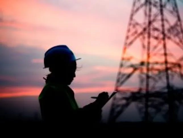 Person taking notes next to an electrical tower at dusk