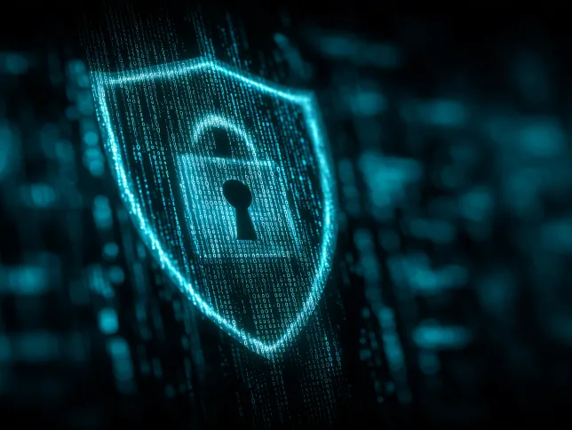 A glowing digital shield with a lock icon at its center symbolizes cybersecurity and data protection, set against a dark background filled with cascading binary code.