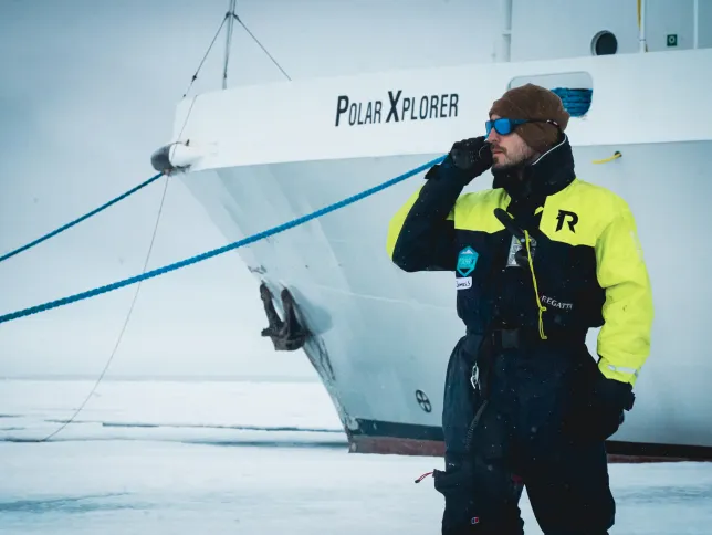 Person in winter clothing holding a device and standing next to a large vessel.