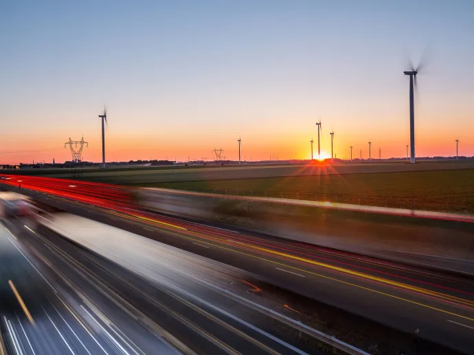 Highway featuring passing cars at sunset, including wind mills in the background