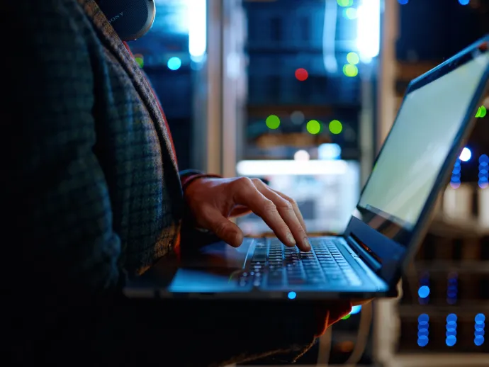 IT technician checking the servers vitals using laptop computer. Male support agent working in a dark network server room