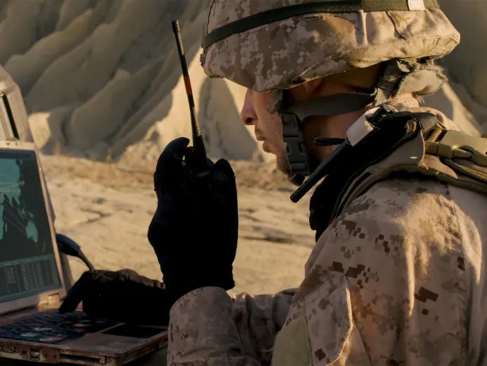 Soldier is using laptop and radio for communication during military operation
