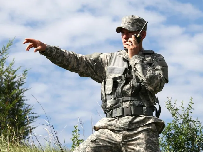 A picture of a soldier talking on a radio and pointing