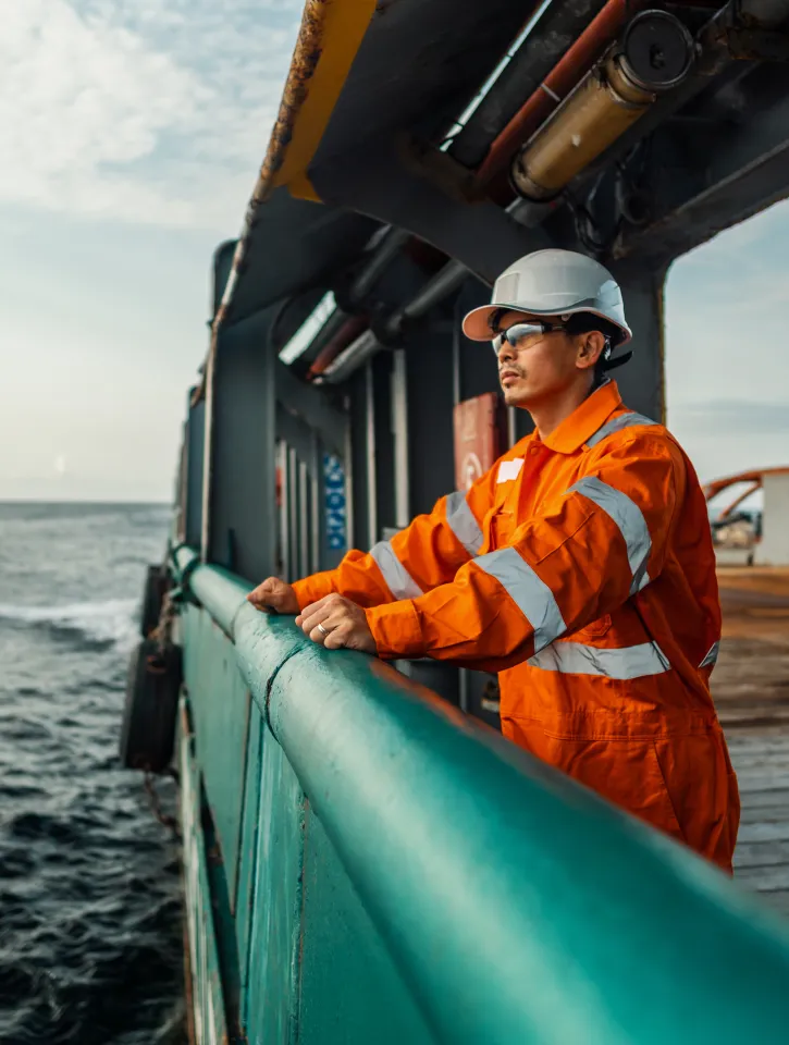 Filipino deck Officer on deck of vessel or ship , wearing PPE personal protective equipment - helmet, coverall, lifejacket, goggles. Safety at sea. He is tired