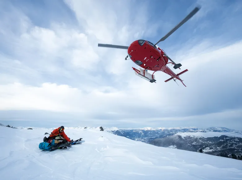 Helicopter in mid-air, picks up backcountry skier from mountain slope, British Columbia