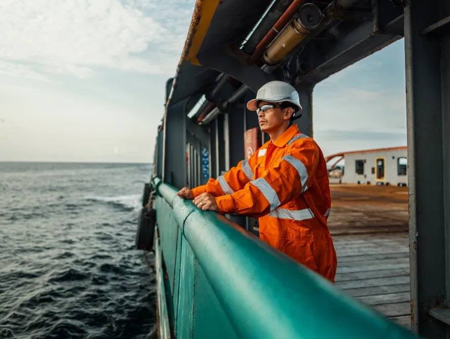 Filipino deck Officer on deck of vessel or ship , wearing PPE personal protective equipment - helmet, coverall, lifejacket, goggles. Safety at sea. He is tired