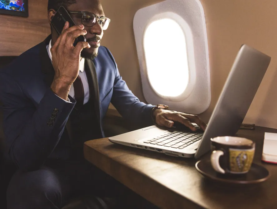 Young attractive and successful African American businessman with glassies talking on the phone and working while sitting in the chair of his private business plane.
