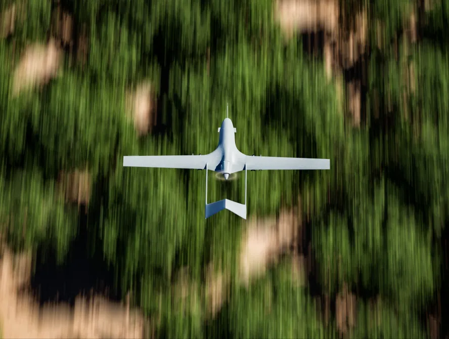 Top shot of a military UAV or drone (Bayraktar TB2) armed with missiles and flying over forest area with the ground blurred