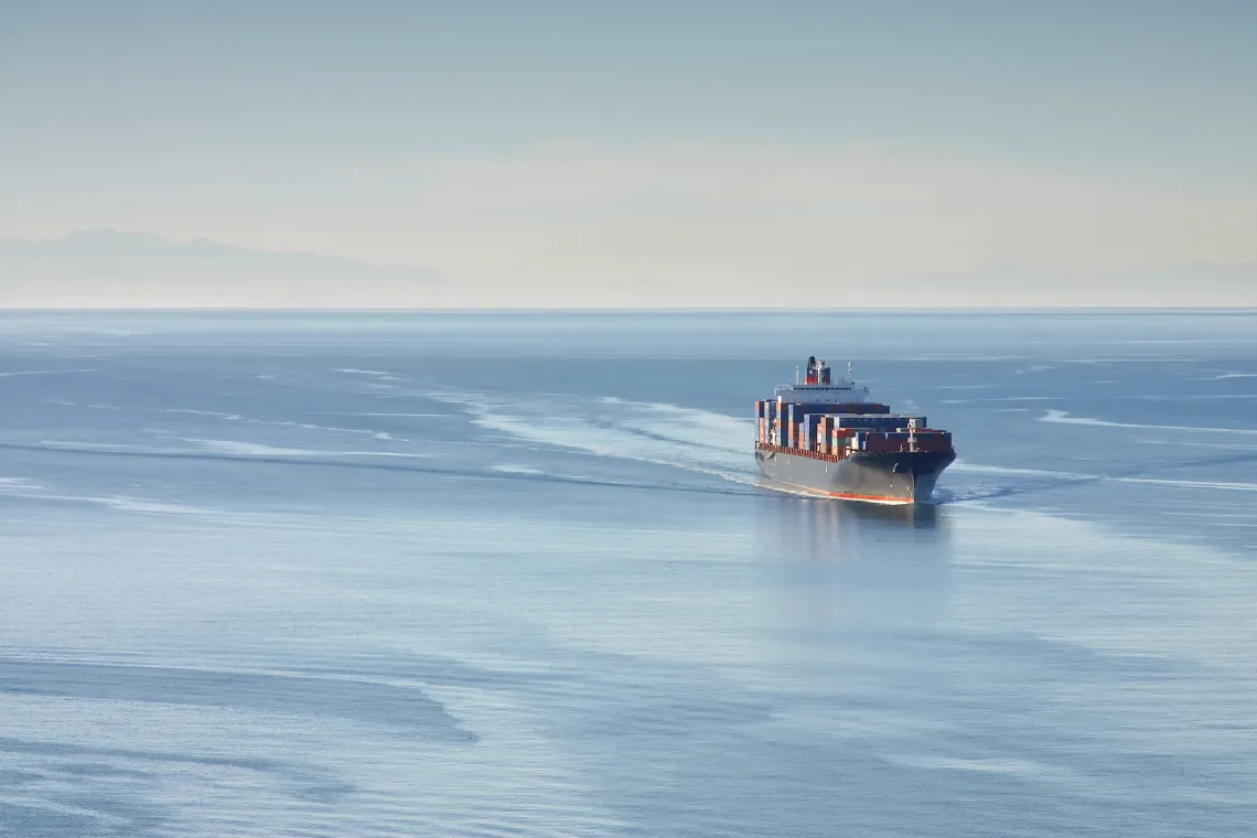 Distant aerial photo of a loaded container ship at sea.