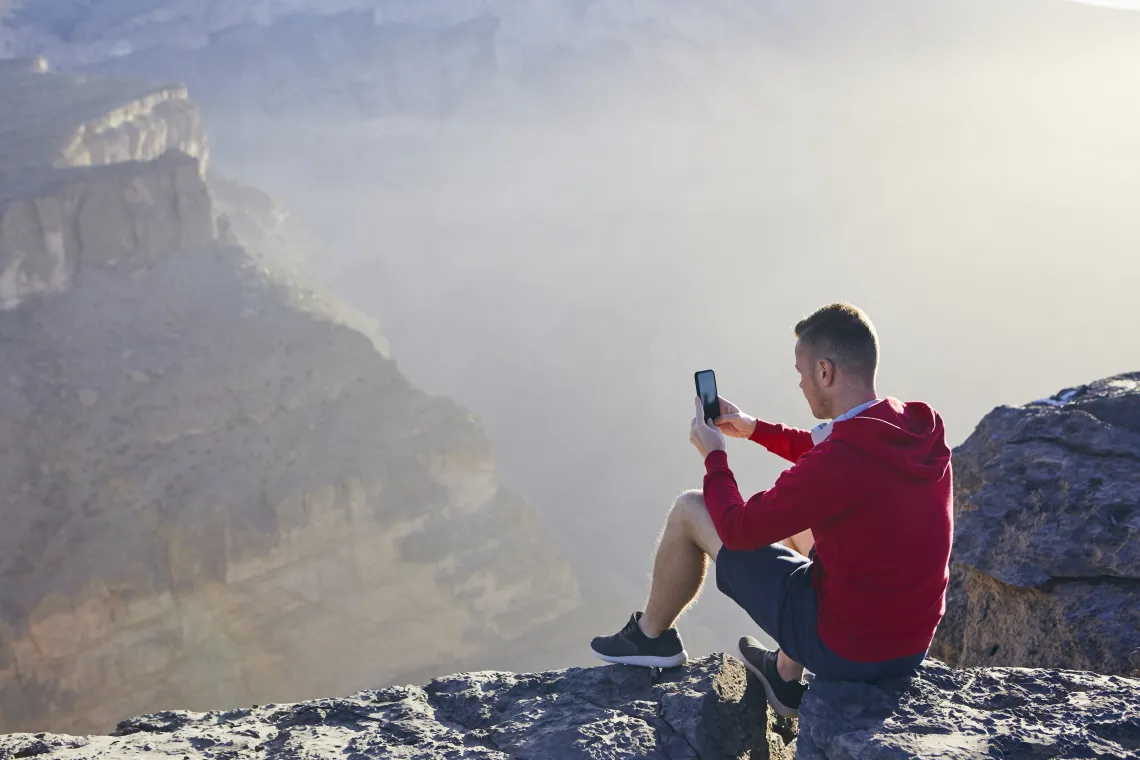 Relaxation in mountains. Young man photographing by mobile phone. Jebel Akhdar, Grand Canyon of Oman.