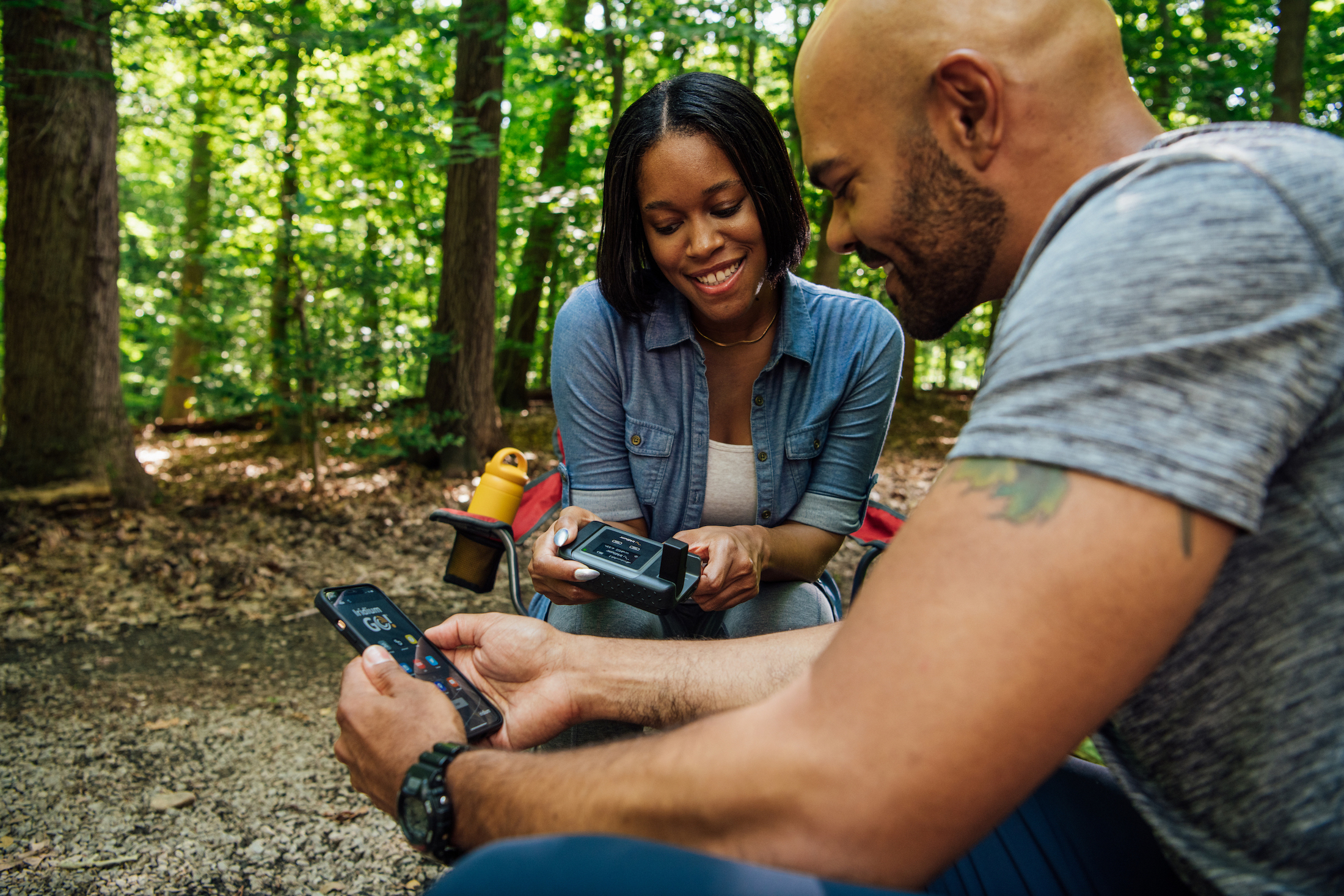 Couple smiling at a campsite in the forest using an Iridium phone