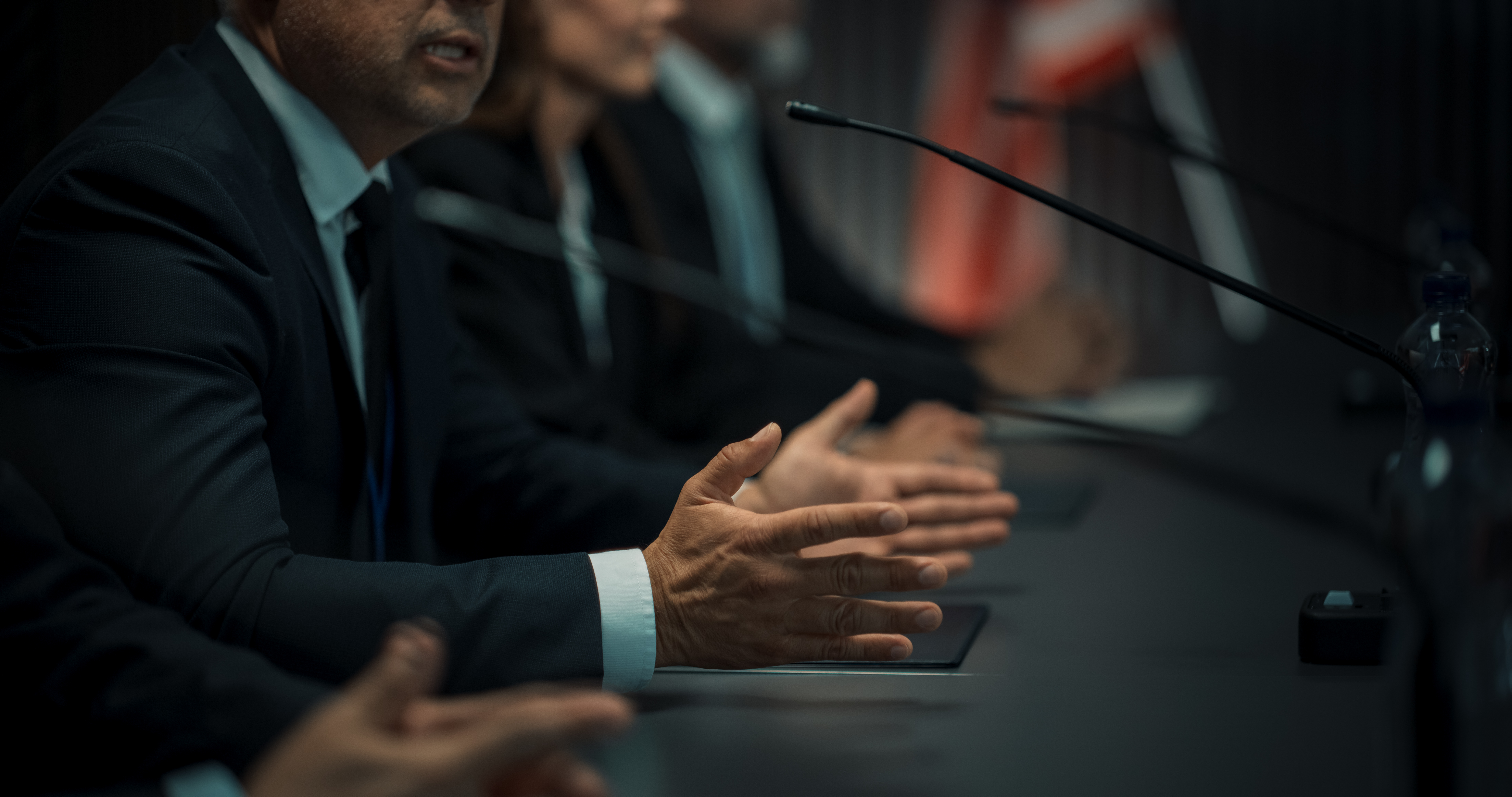 Business professionals speaking at a conference table with microphones.